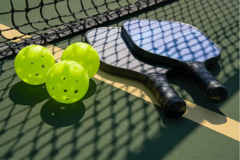 Pickleball paddles and balls on a pickleball court with the net casting a shadow