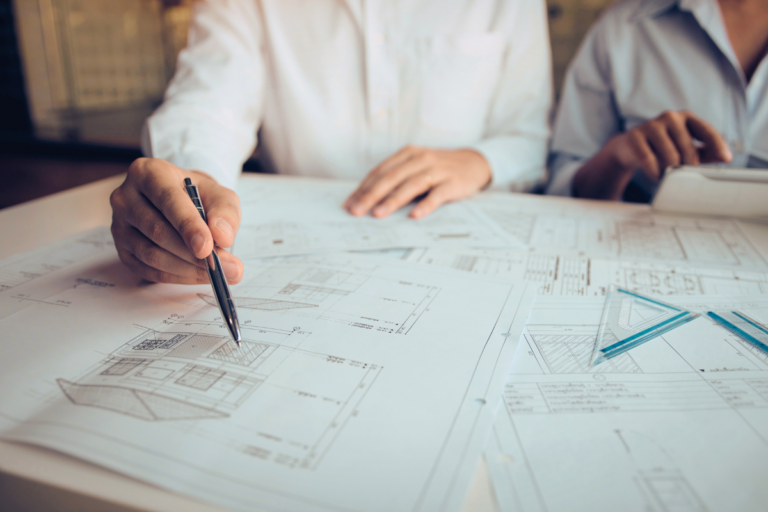 Two sets of hands marking up a set of home floor plan blueprints